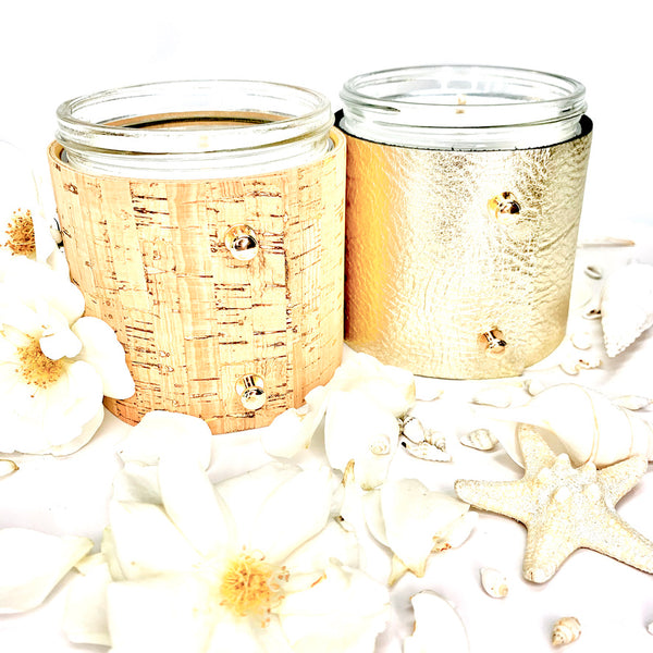 Luxury soy candle gift set in floral and beach scented fragrances, one candle is wrapped in elegant cork with gold inlays and two shiny gold button studs, one candle is wrapped in metallic pale gold leather with two shiny gold button style studs