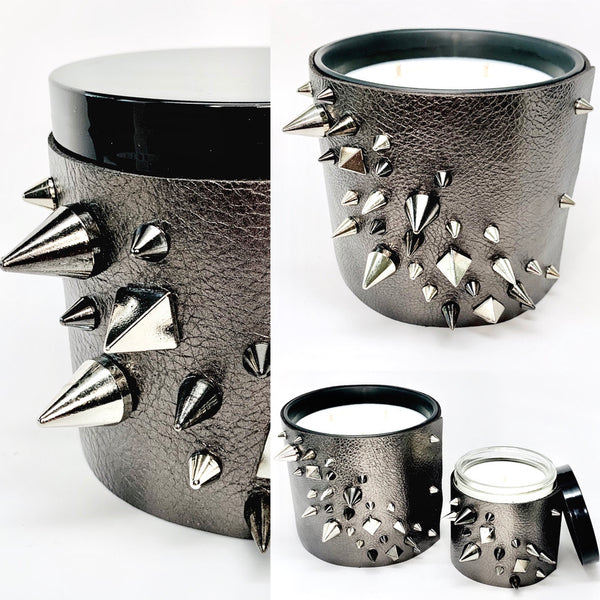 Luxury soy candle with one wick in a metallic gunmetal grey leather sleeve with silver and black studs in a cone and pyramid shape, glass jar underneath the leather with a shiny black lid 