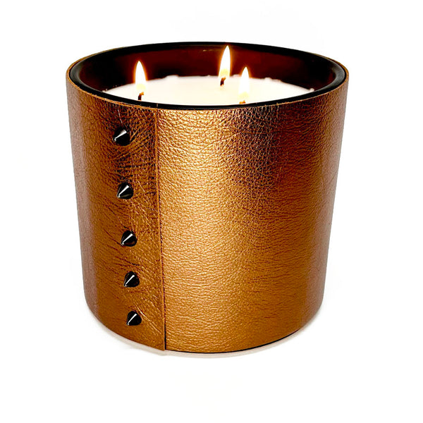 large soy candle with 3 wicks wrapped in a textured metallic bronze leather with 5 cone shaped black studs