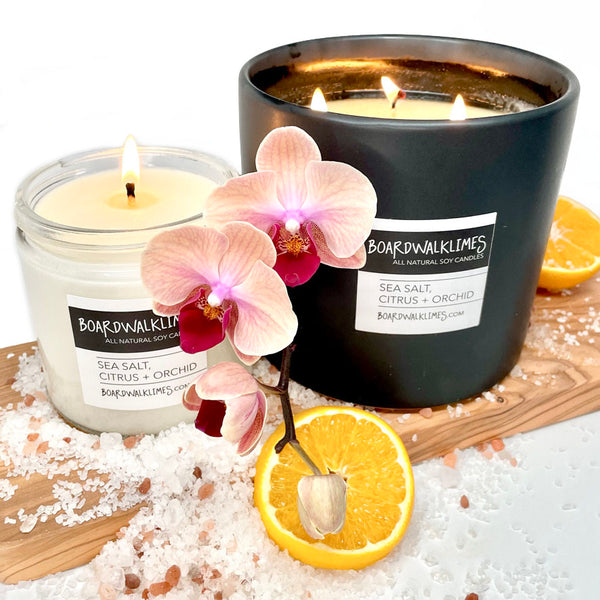 vegan soy candle in a clear glass jar with a shiny black lid filled with floral orchid, citrus, and sea salt fragrances.  A 3 wich large candle in a handmade black ceramic container with floral orchids, sea salt and citrus notes