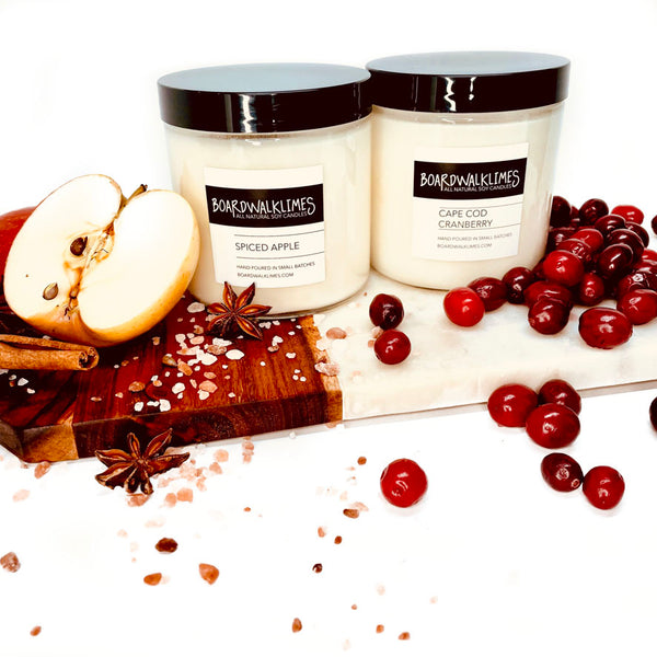 Luxury fall scented soy candles with cotton wicks in glass jars, one is an apple and spice scented candle and one is a cranberry and orange peel scented fall say candle