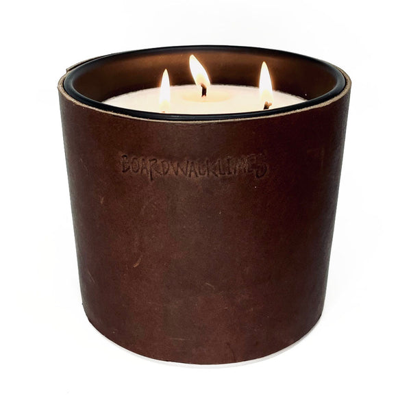 A large 3 wick all natural soy candle is wrapped in a rustic chocolate brown leather sleeve with 3 black button studs