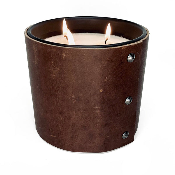 A large 3 wick all natural soy candle is wrapped in a rustic chocolate brown leather sleeve with 3 black button studs