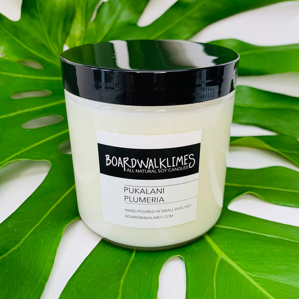 Hawaiian notes of plumeria fill this floral soy candle in a clear glass say with a shiny black modern lid