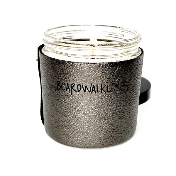 Luxury soy candle with one wick in a metallic gunmetal grey leather sleeve with silver and black studs in a cone and pyramid shape, glass jar underneath the leather with a shiny black lid 