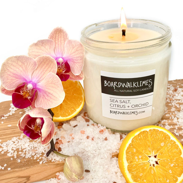 vegan soy candle in a clear glass jar with a shiny black lid filled with floral orchid, citrus, and sea salt fragrances