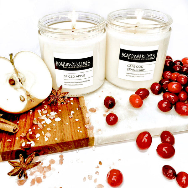 Luxury fall scented soy candles with cotton wicks in glass jars, one is an apple and spice scented candle and one is a cranberry and orange peel scented fall say candle