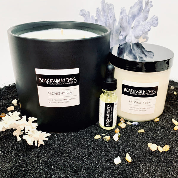 Luxury soy candles and diffuser oils in sea salt and plum beachy summer scented fragrances, one 3-wick large say candles in a handmade black ceramic vase, one 16 oz soy candle in a glass jar with a shiny black lid, one essential oil dropper bottle with a black lid