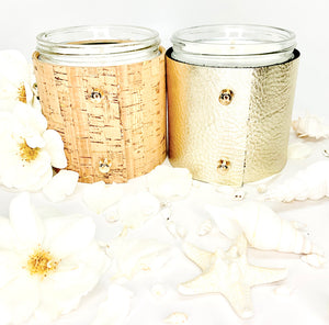 Luxury soy candle gift set in floral and beach scented fragrances, one candle is wrapped in elegant cork with gold inlays and two shiny gold button studs, one candle is wrapped in metallic pale gold leather with two shiny gold button style studs