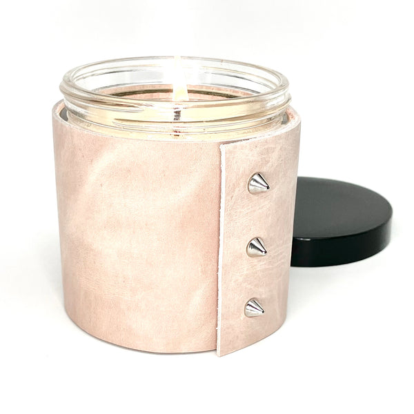An all natural soy candle is wrapped in a pale blush pink leather with 3 silver cone shaped studs