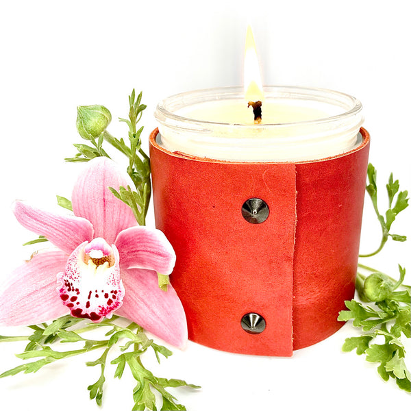An all natural soy candle is wrapped in a red leather with 2 oil rubbed black studs