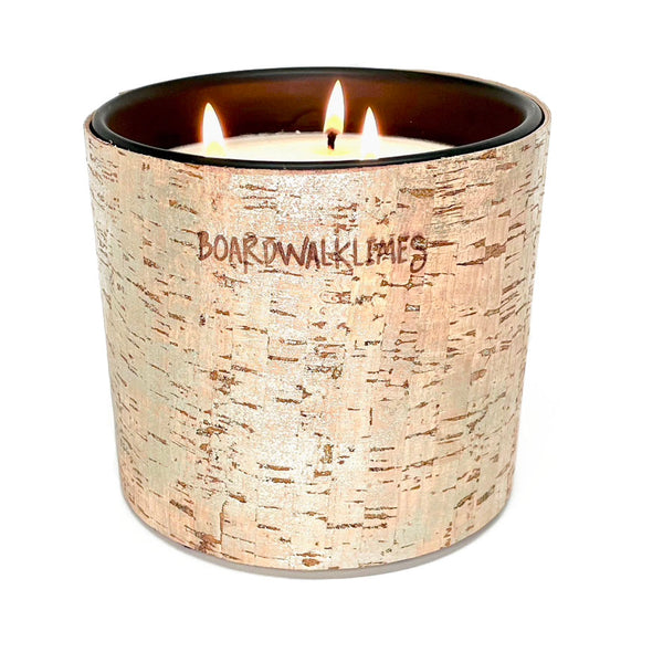A large candle with 3 wicks is wrapped in a cork sleeve covered in a shimmering silver glaze with 5 shiny silver cone shaped studs