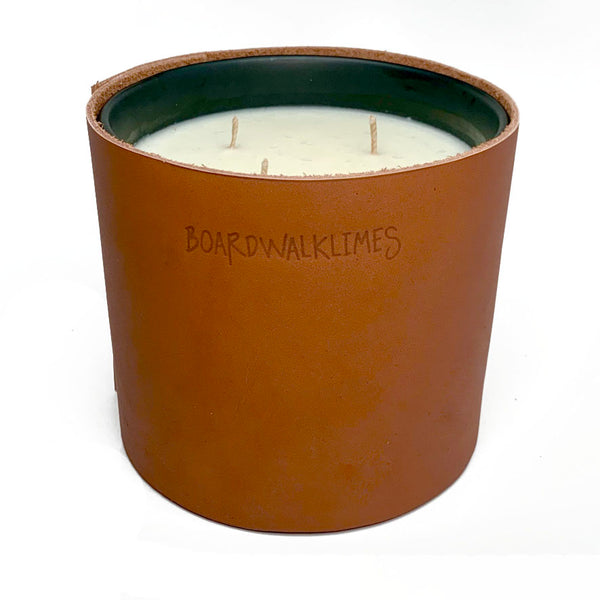 A large 3 wick soy candle is wrapped in a rich caramel colored leather with 3 shiny black cone shaped studs
