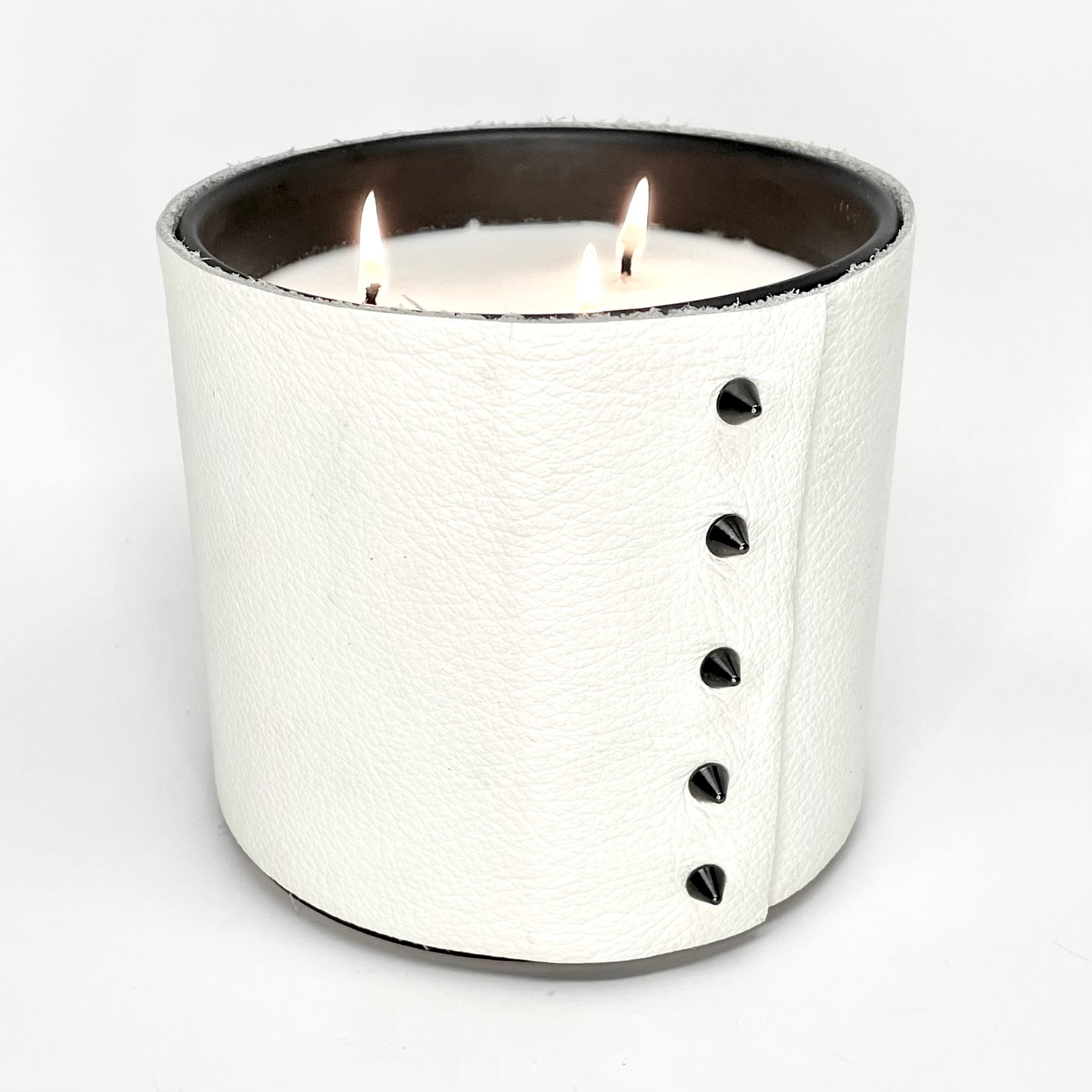 large soy candle with 3 wicks wrapped in a textured white leather with 5 cone shaped black studs