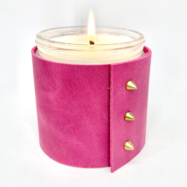 Scented all natural soy candle wrapped in a bright pink leather sleeve with three gold cone shaped studs