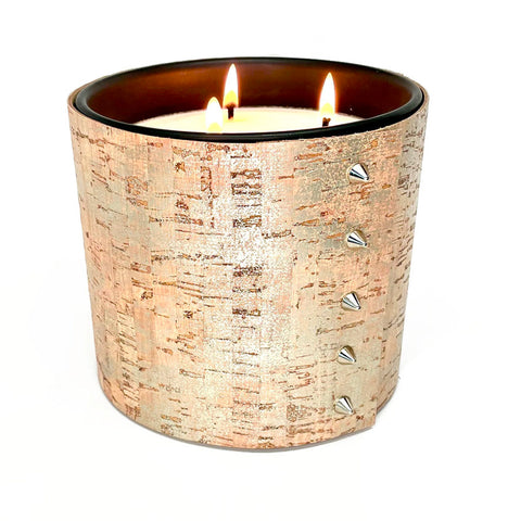 A large candle with 3 wicks is wrapped in a cork sleeve covered in a shimmering silver glaze with 5 shiny silver cone shaped studs