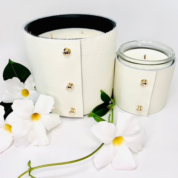 Large Luxury 3-wick Soy Candle in exotic floral and jasmine fragrances in a designer fine white leather wrap with 3 rose gold colored studs and a smaller 1-wick soy candle in fine white leather sleeves