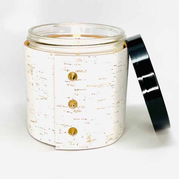 An all natural soy candle is wrapped in a white cork sleeve with 3 gold cone shaped studs