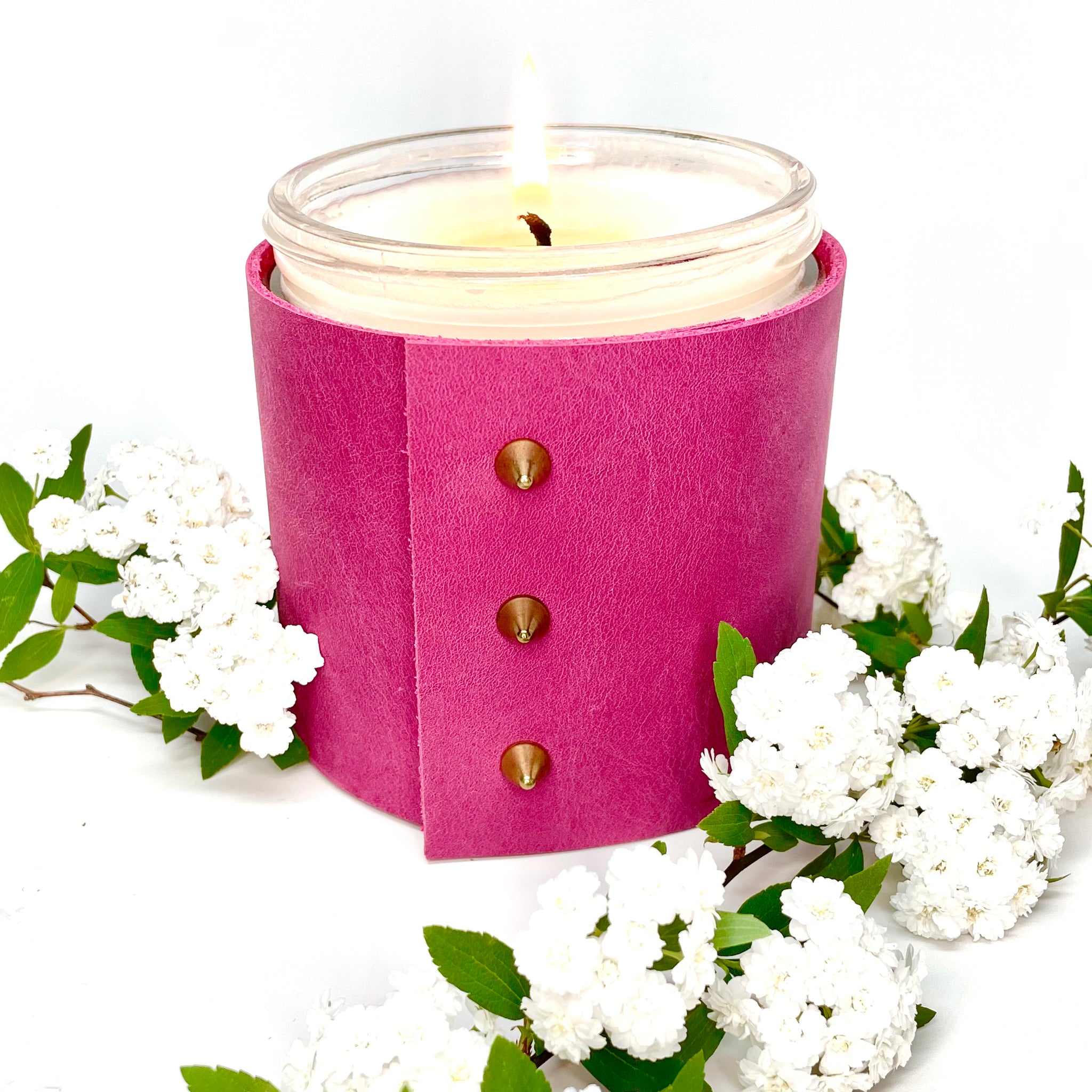 Scented all natural soy candle wrapped in a bright pink leather sleeve with three gold cone shaped studs