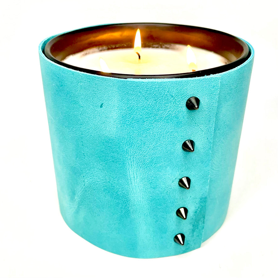 A large 3-wick all natural scented soy candle is wrapped in a bright turquoise leather with 5 black cone shaped studs