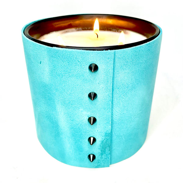 A large 3-wick all natural scented soy candle is wrapped in a bright turquoise leather with 5 black cone shaped studs