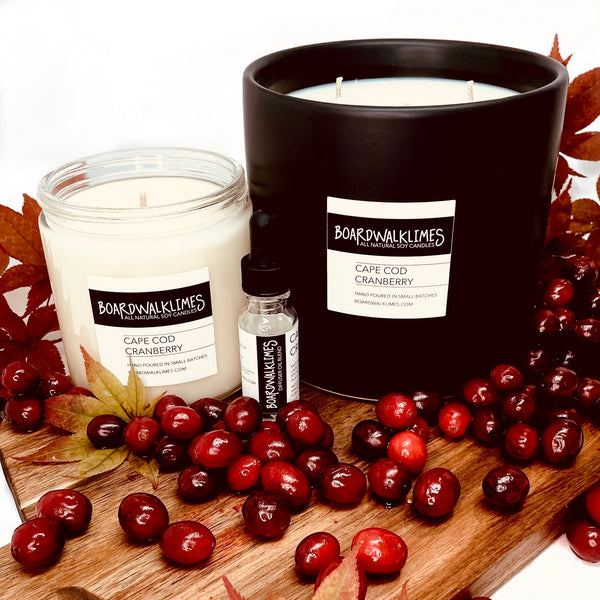 Fall scented luxury soy candles and essential oil diffuser oil in cranberry and orange scents in clear glass jar and a handmade large black ceramic vase for a coffee table candle
