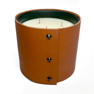 A large 3 wick soy candle is wrapped in a rich caramel colored leather with 3 shiny black cone shaped studs