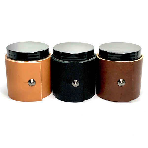 Three 4 oz candles in masculine scents wrapped in dark brown Teton leather, textured black leather, and caramel colored fine leather with oil rubbed black studs