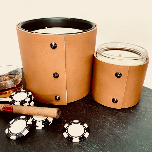 Luxury masculine bourbon, spiced honey, and smoke scented soy candles wrapped in rich caramel colored leather with shiny black button studs