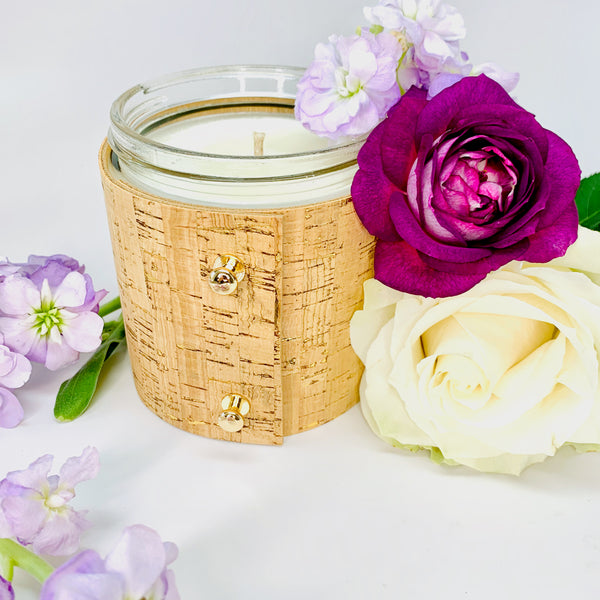 Beautiful floral soy candle with rose, gardenia, and lilac wrapped in a textured cork sleeve with gold inlays and 3 rose gold colored button studs