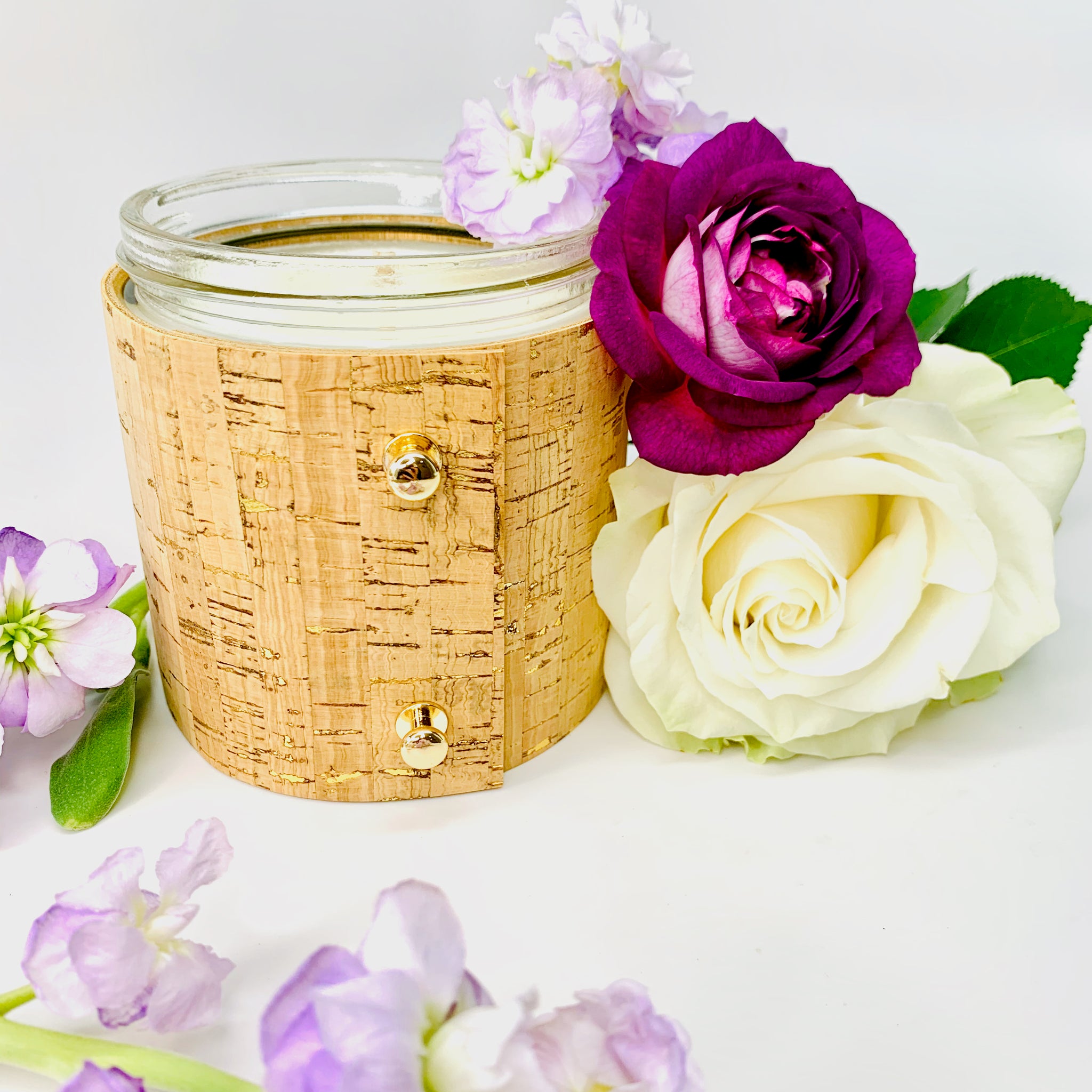 Beautiful floral soy candle with rose, gardenia, and lilac wrapped in a textured cork sleeve with gold inlays and 3 rose gold colored button studs